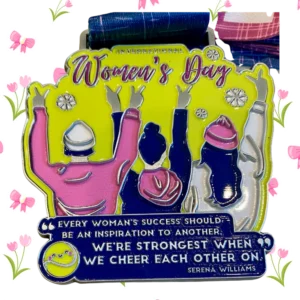 International Women's Day commemorative medal with bright yellow background and silhouettes of women with raised arms in pink, navy, and white colors. The medal features the quote from Serena Williams: 'Every woman's success should be an inspiration to another. We're strongest when we cheer each other on.' The medal includes a blue ribbon and is decorated with pink flower accents around the border.