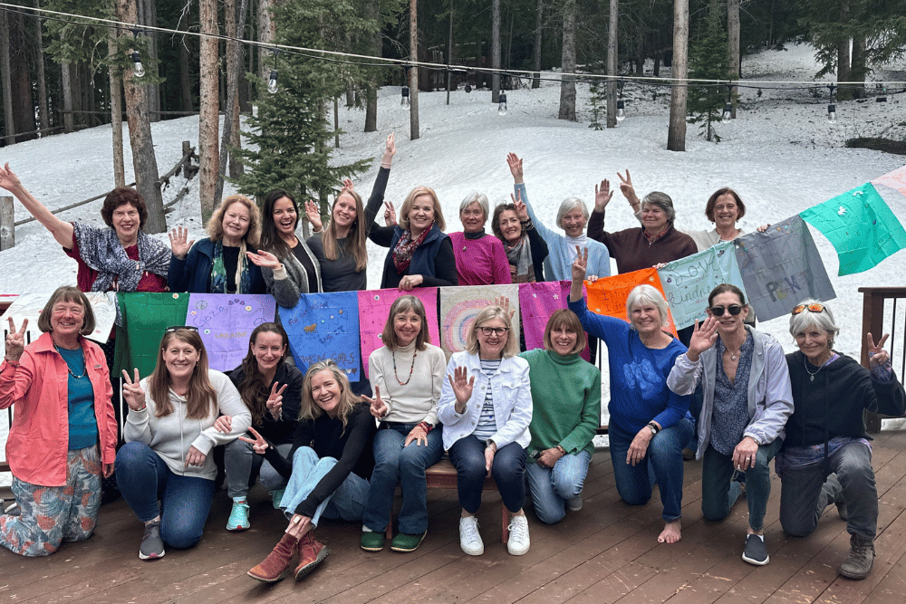 A large group of women smiles while holding international peace flags in a snowy background