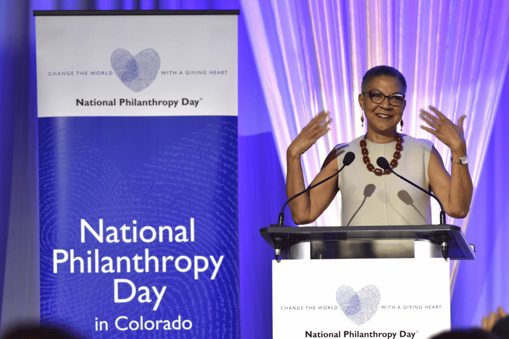 Lauren Y. Casteel stands smiling in front of a podium and next to a banner that reads National Philanthropy Day