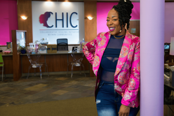 Sadé Cooper, a Black woman in a pink blazer, leans against a pillar next to the sign, CHIC.
