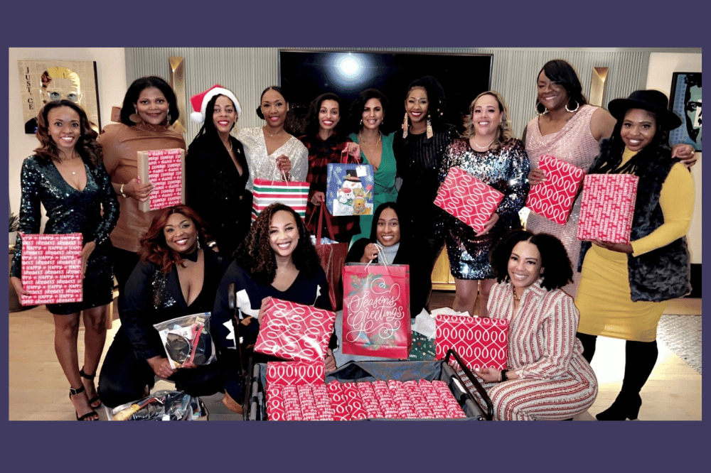 A group of Black women smile at the camera holding wrapped gifts for the holidays.